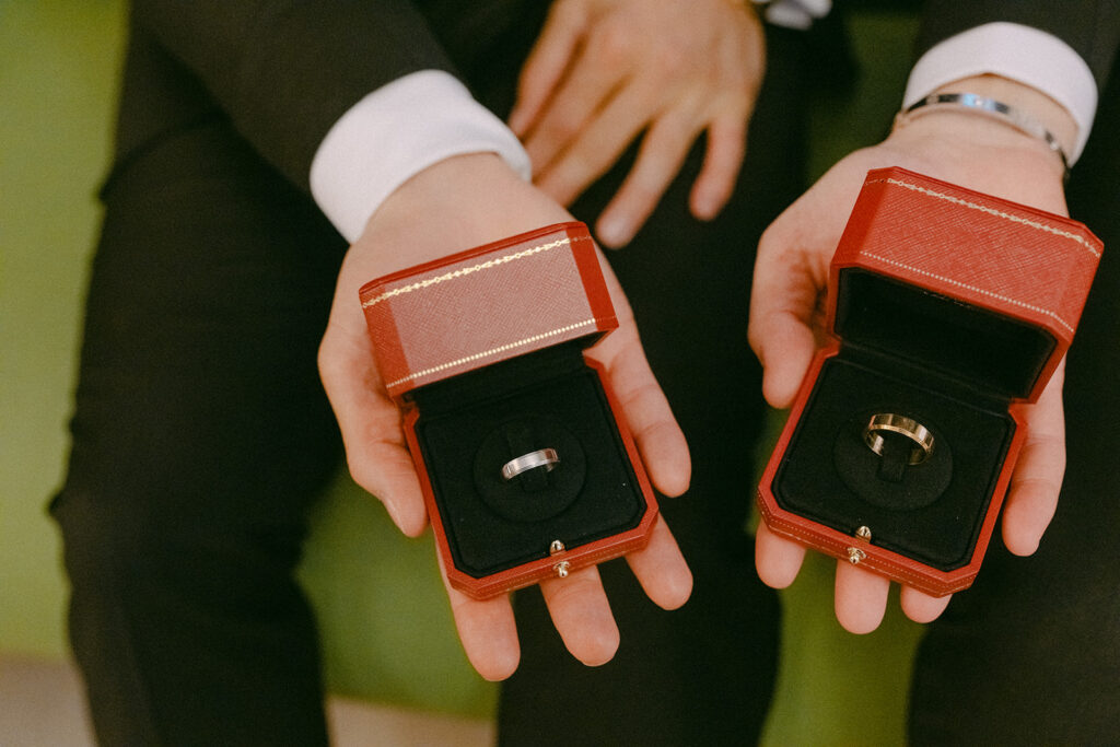 Two grooms holding open red ring boxes